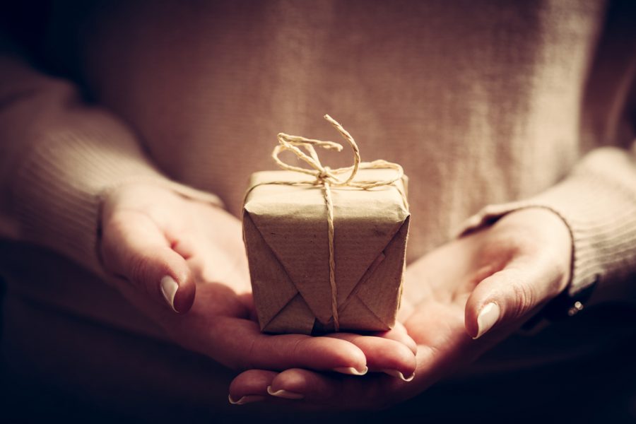 a women's hand holding a gift wrapped in recycled wrapping paper and twine